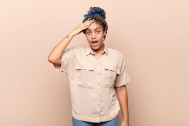 Genç afro kadın mutlu, şaşkın ve şaşırmış görünüyor, gülümsüyor ve inanılmaz ve inanılmaz iyi haberleri fark ediyor.