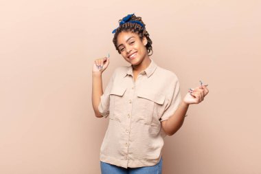 Genç afro kadın gülümsüyor, tasasız hissediyor, rahat ve mutlu, dans ediyor ve müzik dinliyor, bir partide eğleniyor.