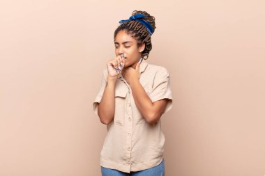 Boğazı ağrıyan ve grip belirtileri gösteren, ağzı kapalı öksüren genç afro bir kadın.