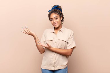 Genç afro kadın gururla ve özgüvenle gülümsüyor, mutlu ve tatmin olmuş hissediyor ve fotokopi alanında bir konsept gösteriyor.