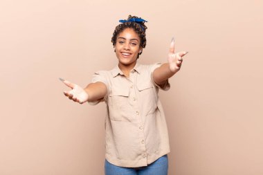 Genç afro kadın neşeyle gülümsüyor sıcak, dostça, sevgi dolu bir kucak veriyor, mutlu ve sevimli hissediyor.