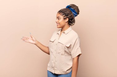 Genç afro kadın gülümsüyor, sizi selamlıyor ve başarılı bir anlaşma için el sıkışmayı teklif ediyor, işbirliği konsepti.