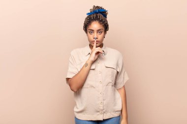 Genç afro kadın ciddi görünüyor ve parmaklarını dudaklarına bastırıp sessizlik ya da sessizlik talep ediyor, sır saklıyor.