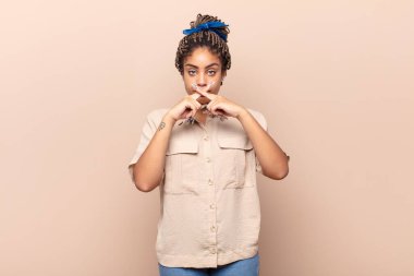 Genç afro kadın ciddi ve hoşnutsuz görünüyor. İki parmağının önde olması reddedilerek sessizlik istiyor.