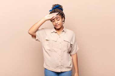 Genç afro kadın stresli, yorgun ve hayal kırıklığına uğramış görünüyor, alnından ter akıyor, umutsuz ve bitkin hissediyor.