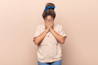 Genç afro kadın üzgün, hayal kırıklığına uğramış, gergin ve depresif, iki eliyle yüzünü kaplayan, ağlayan