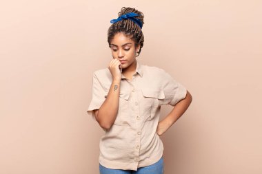 Genç afro kadın ciddi, düşünceli ve endişeli, elleri çenesine bastırılmış, yan bakıyor