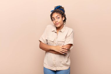 Genç afro bir kadın omuz silkiyor, kafası karışık ve kararsız, kolları bağlı ve şaşkın görünüyor.