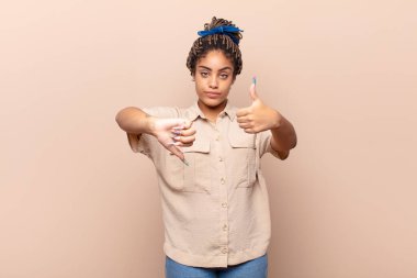 Genç afro kadın kafası karışık, bilgisiz ve kararsız hissediyor, iyi ve kötü seçenekleri ya da seçenekleri tartıyor.