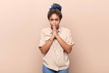 Genç afro kadın endişeli, umutlu ve dindar hissediyor. Avuçlarına bastırılmış, af dileyen sadık bir şekilde dua ediyor.
