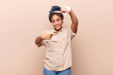 Genç afro kadın mutlu, arkadaş canlısı ve pozitif hissediyor, gülümsüyor ve elleriyle bir portre veya fotoğraf çerçevesi yapıyor.