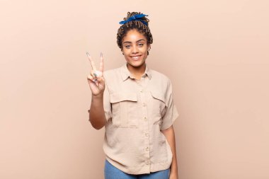 Genç afro kadın gülümsüyor ve arkadaş canlısı görünüyor, iki ya da iki numarayı gösteriyor, elleri önde, geriye doğru sayıyor.