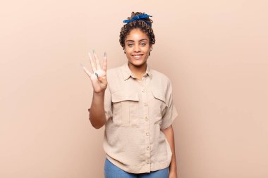 Genç afro kadın gülümsüyor ve arkadaş canlısı görünüyor, 4 ya da 4 numarayı gösteriyor, eli önde, geriye doğru sayıyor.