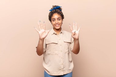 Genç afro kadın gülümsüyor ve arkadaş canlısı görünüyor, 9 ya da 9 numarayı gösteriyor, eli önde, geri sayıyor.