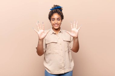 Genç afro kadın gülümsüyor ve arkadaş canlısı görünüyor, onuncu ya da onuncu numarayı gösteriyor, eli önde, geri sayıyor.