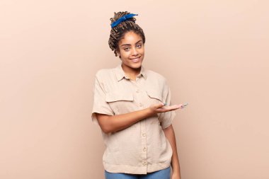 Genç afro kadın neşeyle gülümsüyor, mutlu hissediyor ve fotokopi uzayında bir konsept gösteriyor.