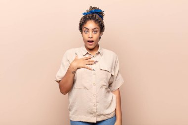 Genç afro kadın şaşkın, şaşkın ve şaşırmış hissediyor, elleri göğsünde ve ağzı açık, kim olduğunu söylüyor, ben?