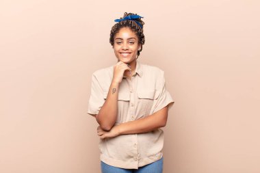 Genç afro kadın gülümsüyor, hayattan zevk alıyor, mutlu, arkadaş canlısı, tatmin olmuş ve tasasız.