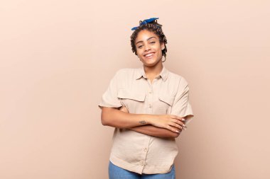 Genç afro kadın kollarını kavuşturup mutlu bir şekilde gülüyor, rahat, pozitif ve tatmin edici bir pozla.