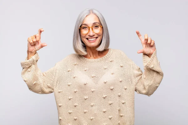 gray haired woman framing or outlining own smile with both hands, looking positive and happy, wellness concept