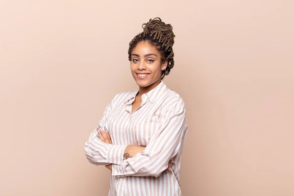 young afro woman smiling to camera with crossed arms and a happy, confident, satisfied expression, lateral view