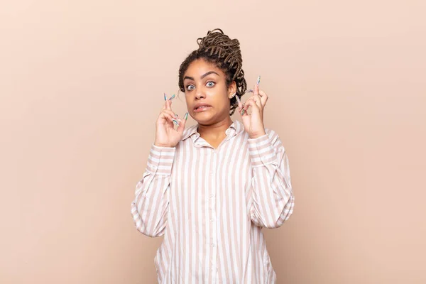 young afro woman crossing fingers anxiously and hoping for good luck with a worried look