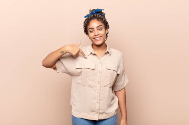 Genç afro kadın mutlu, gururlu ve şaşırmış görünüyor, neşeli bir şekilde kendini gösteriyor, kendinden emin ve kibirli hissediyor.