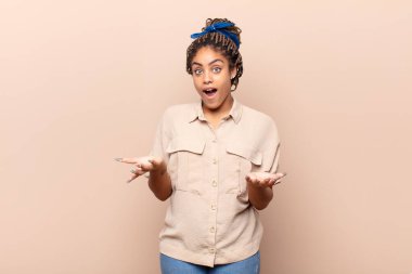 Genç afro kadın ağzı açık ve şaşkın, şok olmuş ve hayretler içinde inanılmaz bir sürprizle