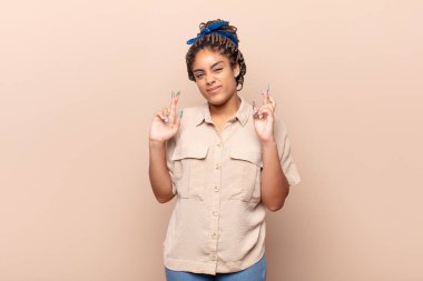 Genç afro kadın endişeyle dua ediyor ve endişeli bir bakışla iyi şanslar diliyor.