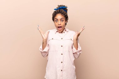 Genç afro kadın mutlu ve heyecanlı görünüyor. Beklenmedik bir sürprizle şoke olmuş. İki eli de açık.