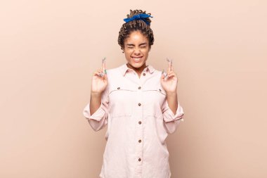 Genç afro kadın gülümsüyor ve endişeyle iki parmağını çapraz yapıyor. Endişeli ve iyi şanslar diliyor.