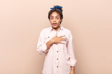 Genç afro kadın şok olmuş ve şaşırmış hissediyor, gülümsüyor, el ele tutuşuyor, o olmaktan mutlu ya da minnettarlık gösteriyor.