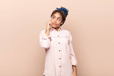 Yoğunlaşmış bakışlı, şüpheli bir ifadeyle, yukarı ve yana bakan genç afro bir kadın.