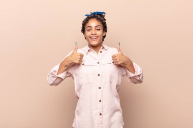 Genç afro kadın mutlu, pozitif, kendinden emin ve başarılı bir şekilde gülümsüyor.