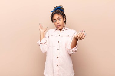 young afro woman shrugging with a dumb, crazy, confused, puzzled expression, feeling annoyed and clueless