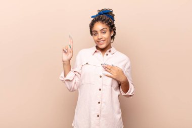 Genç afro kadın mutlu, kendinden emin ve güvenilir görünüyor, gülümsüyor ve zafer işareti gösteriyor, olumlu bir tavırla.