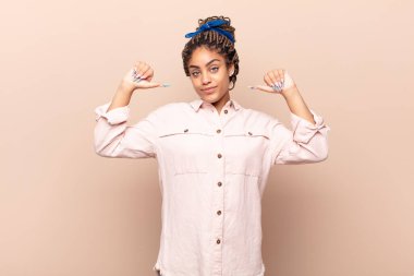 Genç afro kadın gururlu, kibirli ve kendinden emin, tatmin olmuş ve başarılı görünüyor, kendini işaret ediyor.