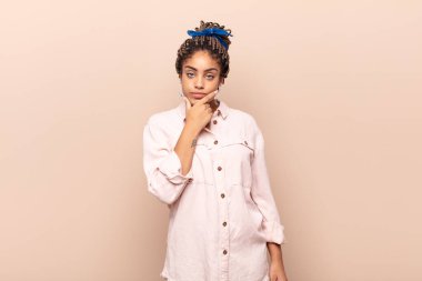 Genç afro kadın ciddi, düşünceli ve güvensiz görünüyor, bir kolu çapraz ve çene üzerinde, seçenekleri tartıyor