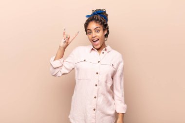 Genç afro kadın kendini mutlu, eğlenceli, kendinden emin, pozitif ve asi hissediyor, elle kaya veya heavy metal işareti yapıyor.