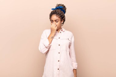 Genç afro kadın iğreniyor, kötü ve nahoş bir koku duymamak için burnunu tutuyor.
