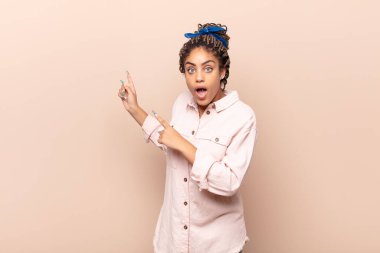 Genç afro kadın şaşkın ve şaşırmış hissediyor, fotokopi alanını işaret ediyor, şaşkın, açık ağızlı bir bakışla