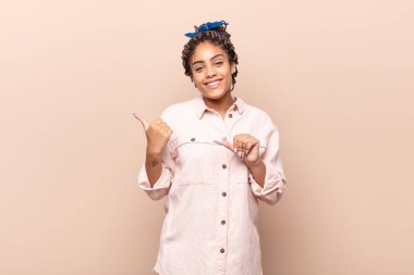 Genç afro kadın neşeyle gülümsüyor ve yan taraftaki fotokopi alanını gösteriyor, mutlu ve tatmin olmuş hissediyor.