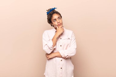 Genç afro kadın düşünceli, meraklı ya da hayal kuruyor, hayal kuruyor ve uzayı kopyalamak için yukarı bakıyor.