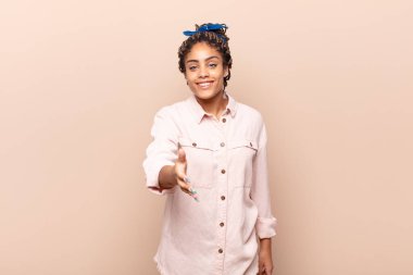 Genç afro kadın gülümsüyor, mutlu görünüyor, kendinden emin ve arkadaş canlısı, bir anlaşma yapmak için el sıkışma teklif ediyor, işbirliği yapıyor.