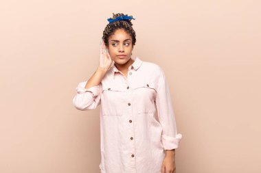 Genç afro kadın ciddi ve meraklı görünüyor, dinliyor, gizli bir konuşma veya dedikodu duymaya çalışıyor, kulak misafiri oluyor.