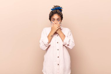 Genç afro kadın şok olmuş, şaşırmış bir ifadeyle ağzını kapatıyor, sır saklıyor ya da 