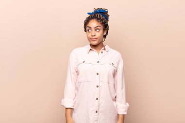 Genç afro kadın şaşkın, mutlu, şaşkın ve şaşırmış hissediyor, ağzı açık bir şekilde yana bakıyor.