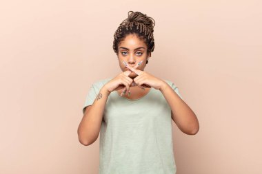 Genç afro kadın ciddi ve hoşnutsuz görünüyor. İki parmağının önde olması reddedilerek sessizlik istiyor.
