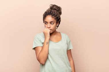 Genç afro kadın ciddi, düşünceli ve endişeli, elleri çenesine bastırılmış, yan bakıyor