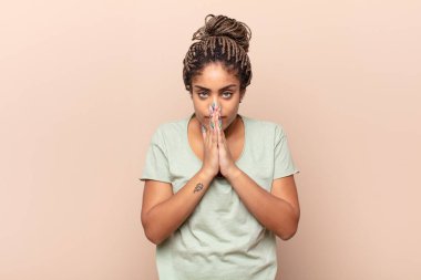 Genç afro kadın endişeli, umutlu ve dindar hissediyor. Avuçlarına bastırılmış, af dileyen sadık bir şekilde dua ediyor.